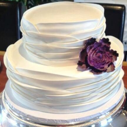 Tiered cake with ruffled icing and a purple flower